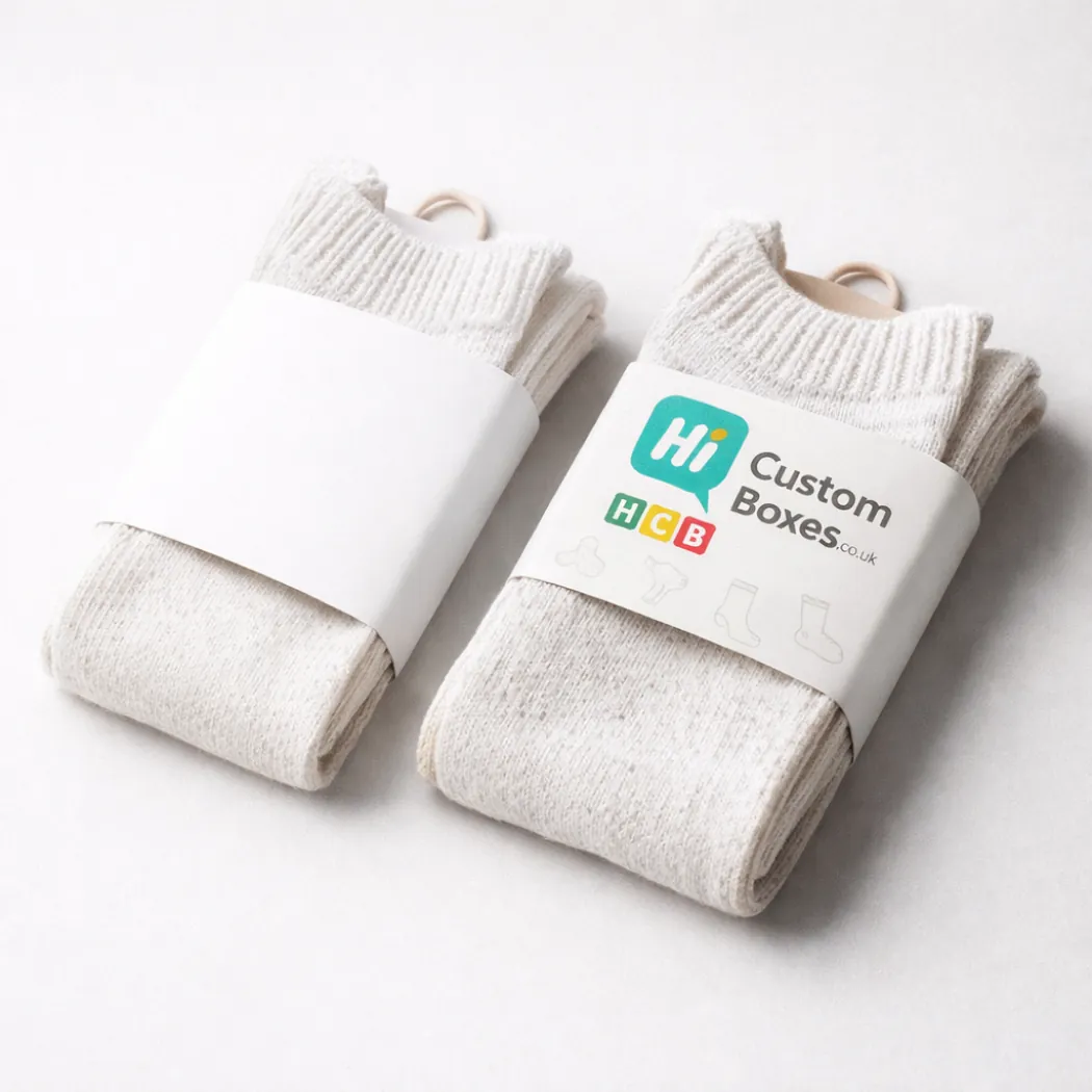 Two pairs of cream-coloured woollen socks held together by branded white paper belly band wraps- class=